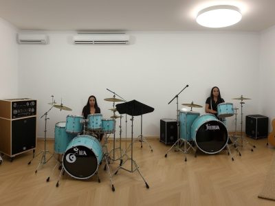 Imagem de estudantes em aula de música, tocando instrumentos musicais e estudando teoria musical.