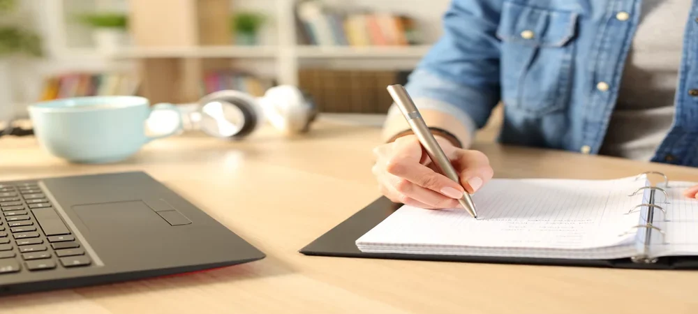 uma pessoa escrevendo em um caderno sobre curiosidades da língua portuguesa