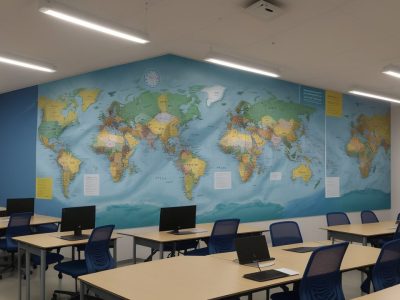 Professor e alunos em sala de aula, colaborando em um projeto de planejamento de aula interdisciplinar, com foco em exemplos práticos e engajamento.