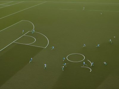 Imagem de um campo de futebol com jogadores executando táticas de treinamento, ilustrando a teoria do futebol na prática.