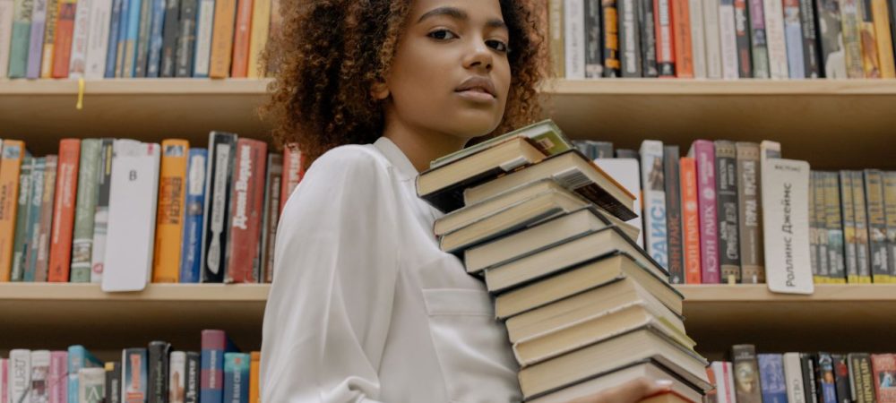 pessoa trabalhando como auxiliar de biblioteca e carregando livros, próxima a prateleiras