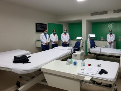 Profissional de saúde de jaleco conversa com paciente em sala de atendimento, representando a ética na saúde com livros de bioética ao fundo.