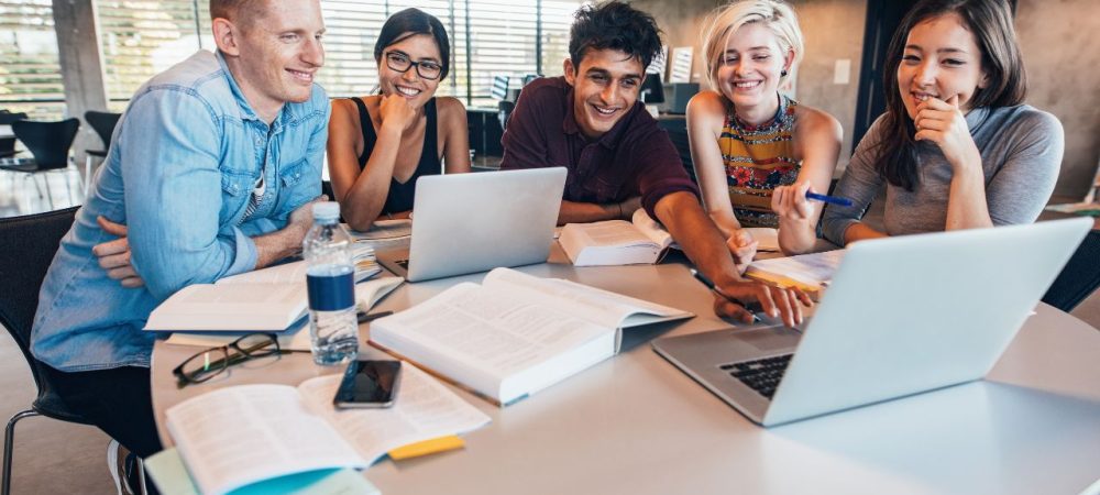 Estudantes pesquisando em laptop sobre horas complementares para cumprir exigência da faculdade com cursos online.