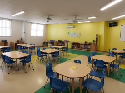 Sala de aula inclusiva com crianças aprendendo, professor utilizando recursos visuais e audiovisuais, ambiente acolhedor para TDAH.