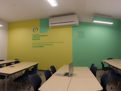 Alunos diversificados em sala de aula moderna, utilizando tecnologia e colaborando em atividades sob supervisão pedagógica.